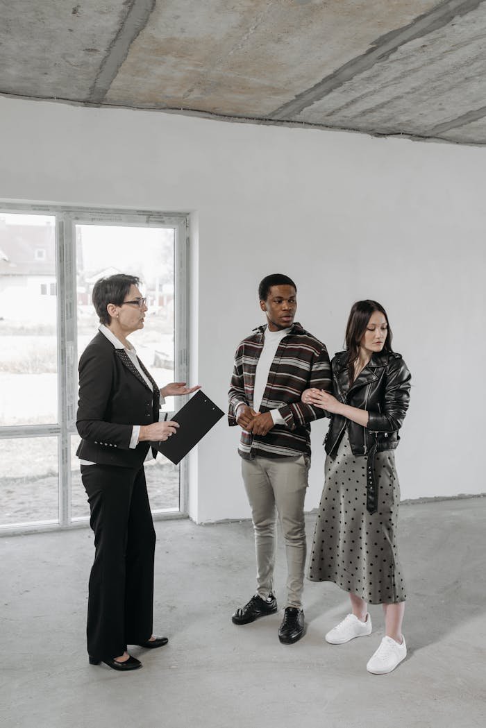 Multicultural couple discussing potential house purchase with realtor inside an empty room.