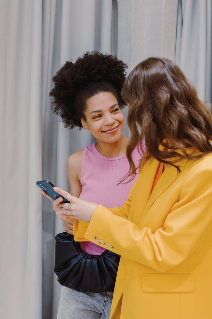 Two women shopping and smiling while using a smartphone indoors.